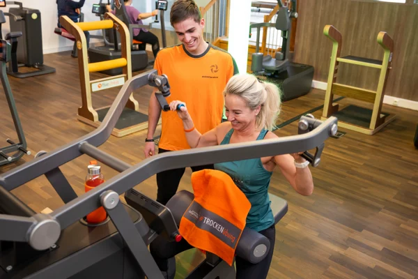 Trainer betreut eine Kundin beim Krafttraining am Gerät