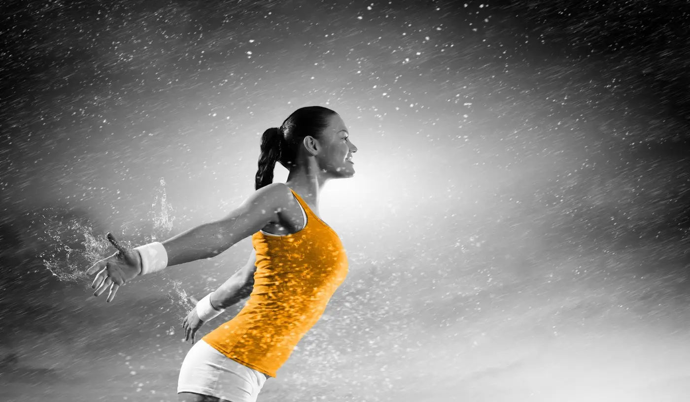 Eine Frau im orangen Top streckt die Arme nach hinten, um sie herum spritzt Wasser