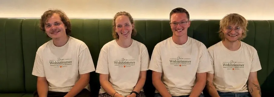 Luk, Lilli, Pascal und Martin, das Team von Dein Wohnzimmer, sitzen lachend auf dem grünen Sofa